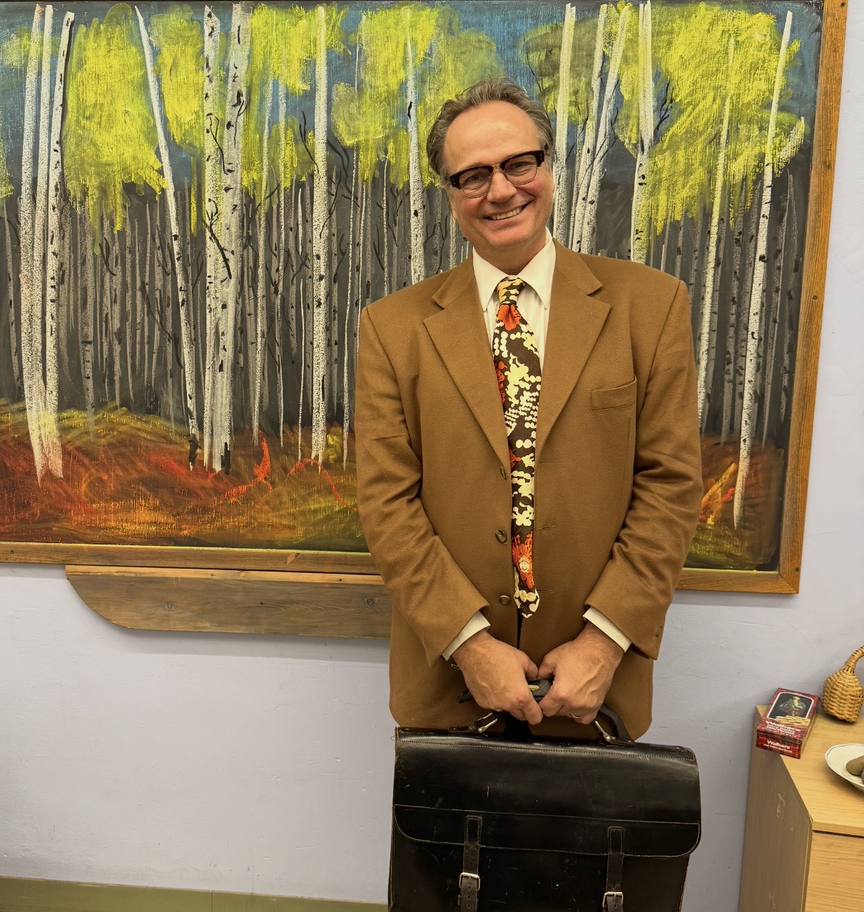 Timothy smiling in a suit in front of a painted forest